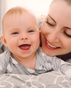 happy smiling mother and baby playing on bed at home